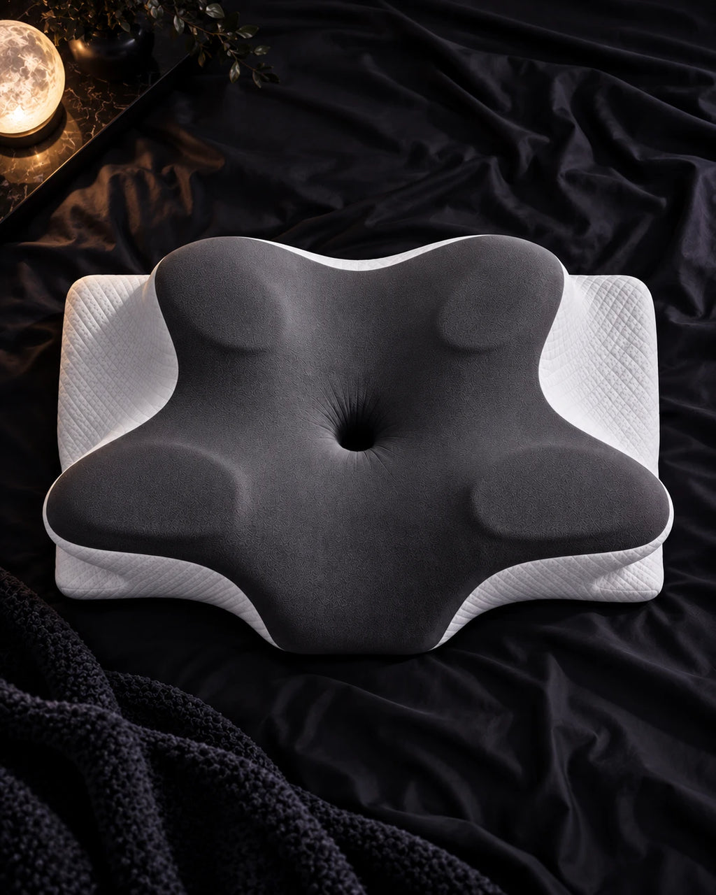 Top-down view of the Norevane pillow on black sheets beside a moon lamp